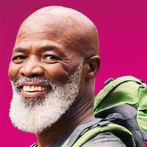 A Black man with a gray beard and a backpack smiles at the camera