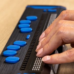 Fingers resting on a Braille display that features large, blue buttons.